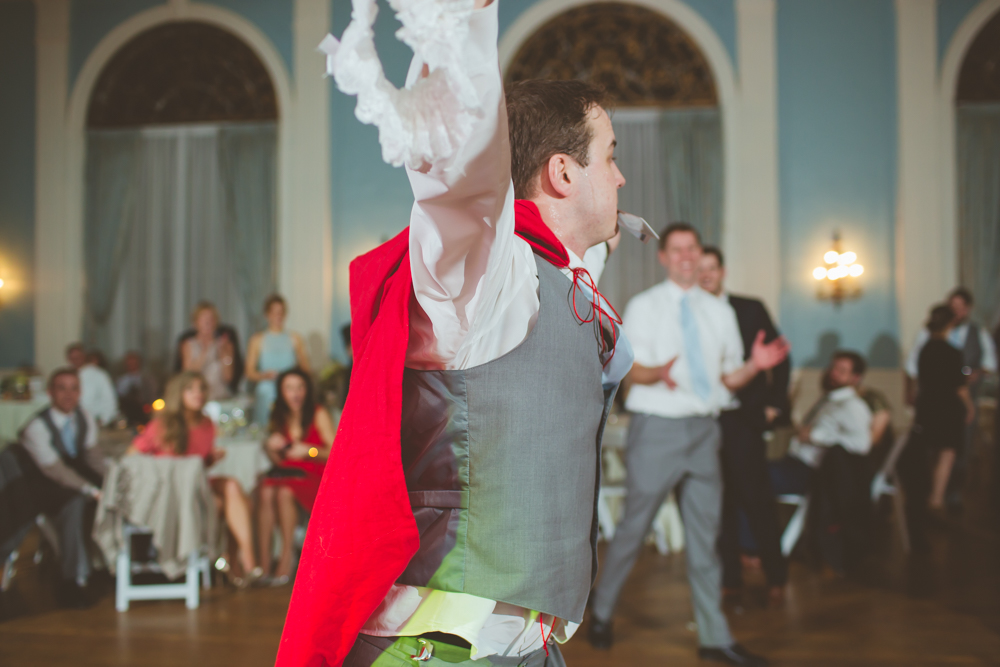 groomsman in a cape doing a flip to catch the garter