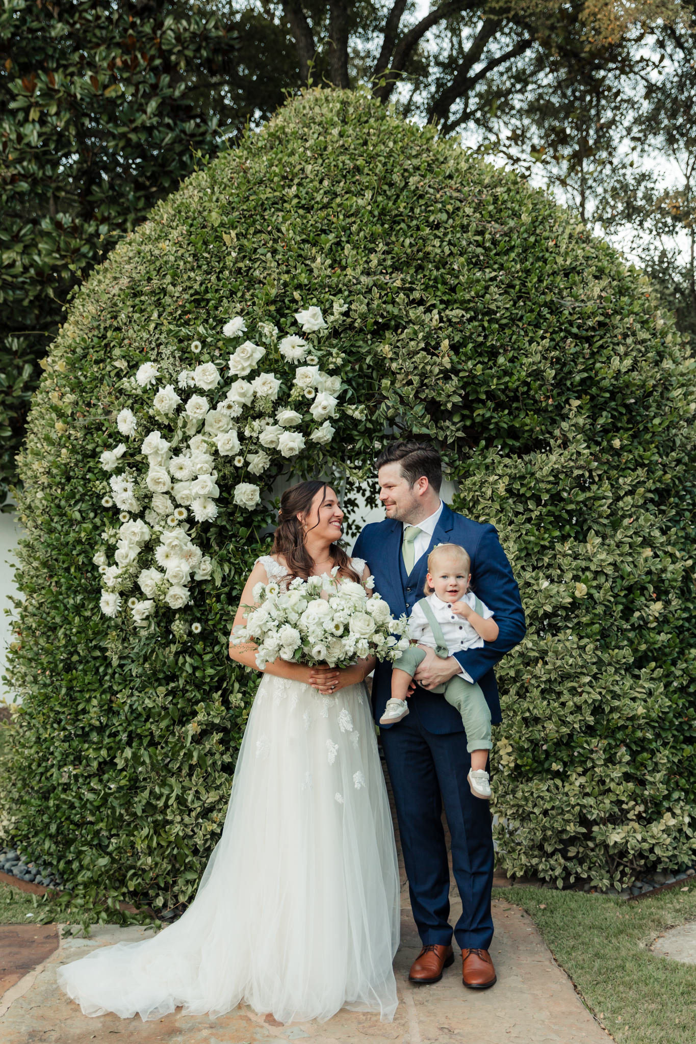 bride and groom with their son in front of ceremony arch