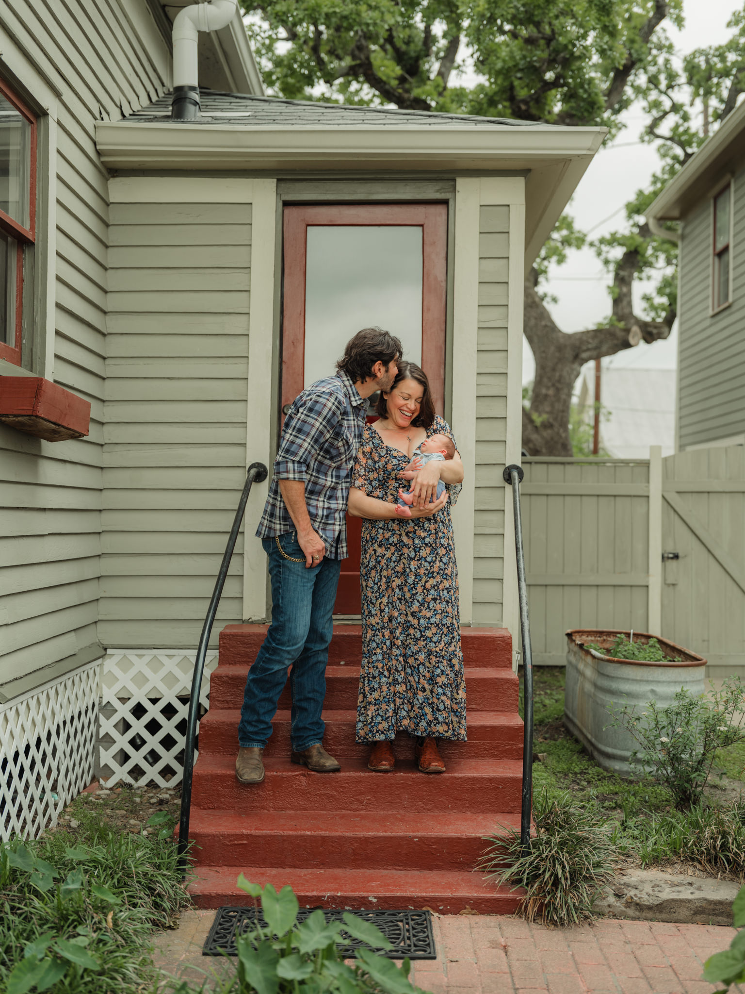 holding baby and kissing wife on the porch